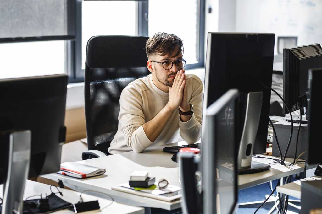 Programmer sitting at the desk in his office and trying to solve problem of new code.