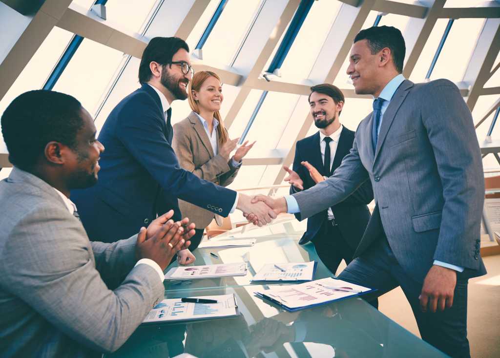 Group of business people congratulating their handshaking colleagues after signing contract